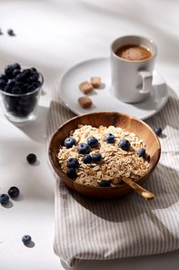 food, eating and breakfast concept - oatmeal in wooden bowl with blueberries and spoon, cup of coffee on kitchen towel