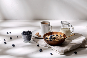 food, eating and breakfast concept - oatmeal in wooden bowl with blueberries, milk in glass jug and cup of coffee with brown sugar on kitchen towel