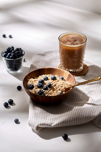 food, drinks and breakfast concept - oatmeal in wooden bowl with blueberries and spoon, glass of ice coffee on cork drink coaster and kitchen towel