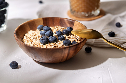 food, healthy eating and breakfast concept - close up of oatmeal in wooden bowl with blueberries and spoon
