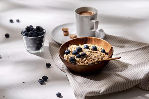 food, eating and breakfast concept - oatmeal in wooden bowl with blueberries and spoon, cup of coffee on kitchen towel