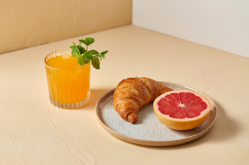 food and eating concept - glass of orange juice with peppermint, croissant and grapefruit on plate for breakfast