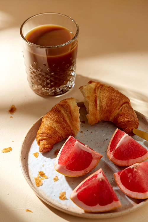 food, drink and eating concept - glass of coffee, croissant and grapefruit on plate for breakfast