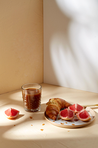 food, drink and eating concept - glass of coffee, croissant and grapefruit on plate for breakfast