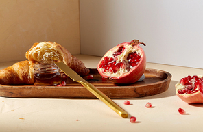 food and eating concept - croissant, pomegranate and honey with table knife on wooden tray