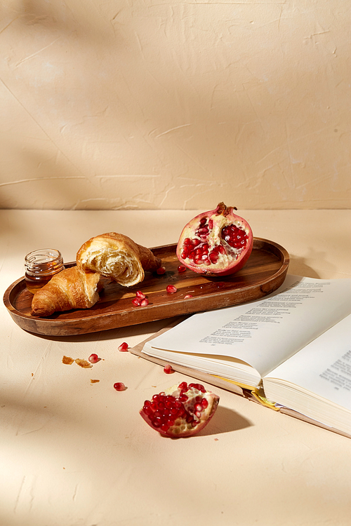 food and eating concept - open book, croissant, pomegranate and honey on wooden tray
