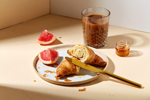 food, drink and eating concept - glass of coffee, honey, croissant and grapefruit on plate for breakfast