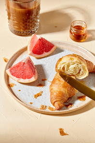 food, drink and eating concept - glass of coffee, honey, croissant and grapefruit on plate for breakfast