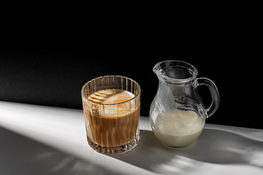caffeine, objects and drinks concept - glass of coffee and jug with milk or cream on table