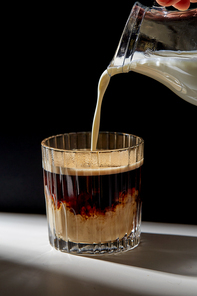caffeine and drinks concept - hand with jug pouring cream or milk to glass of coffee on table
