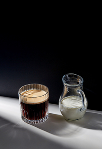 caffeine, objects and drinks concept - glass of coffee and jug with milk or cream on table
