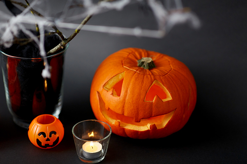 halloween and holiday concept - jack-o-lantern or carved pumpkin, burning candles and spider web decoration