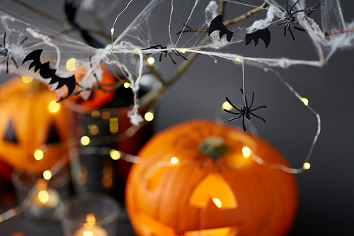 halloween and holiday decorationsconcept - jack-o-lantern or carved pumpkin, burning candles, electric garland string, spiders and bats on spiderweb