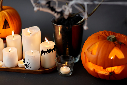 halloween and holiday decorations concept - jack-o-lantern or carved pumpkin, burning candles, spiders and bats on spiderweb