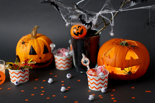 halloween and holiday decorations concept - jack-o-lantern or carved pumpkin, candies in paper cups and spiders