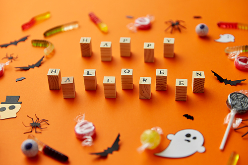 halloween and holiday concept - wooden toy blocks with trick or treat lettering candies and decorations on orange background