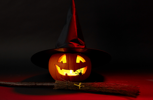 halloween and holiday decorations concept - jack-o-lantern in witch's hat with spider and broom in darkness