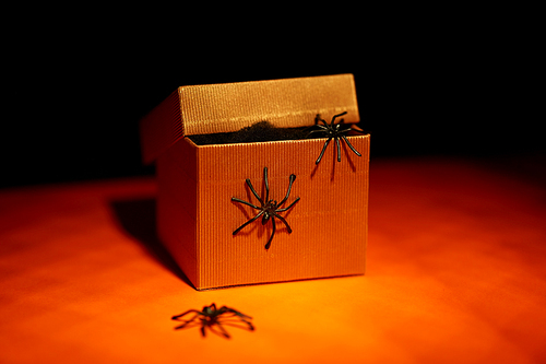 halloween, holidays and party concept - toy spiders crawling out of gift box on orange background