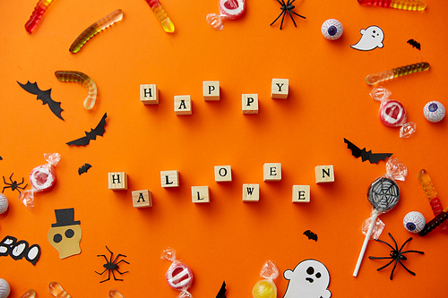 halloween and holiday concept - wooden toy blocks with trick or treat lettering candies and decorations on orange background