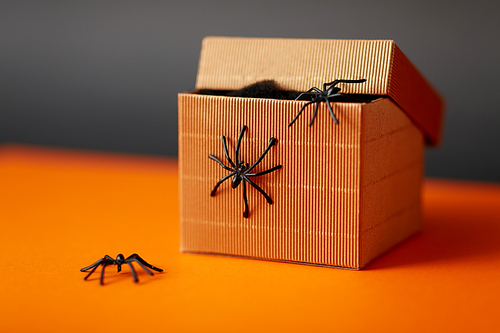halloween, holidays and party concept - toy spiders crawling out of gift box on orange background