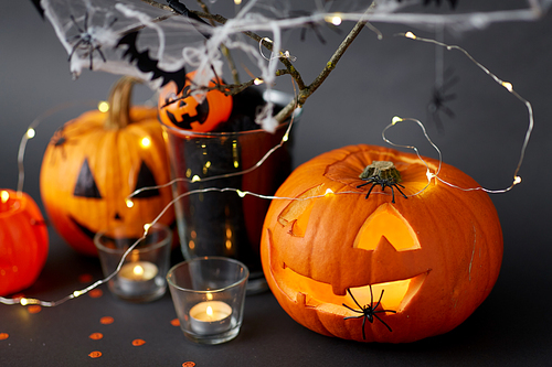 halloween and holiday decorationsconcept - jack-o-lantern or carved pumpkin, burning candles, electric garland string, spiders and bats on spiderweb