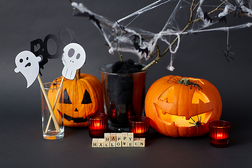 holidays and decorations concept - wooden toy blocks with happy halloween letters, jack-o-lanterns or carved pumpkins, burning candles and spiders on spiderweb