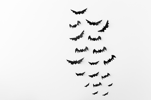 halloween, decoration and scary concept - flock of black paper bats flying over white background