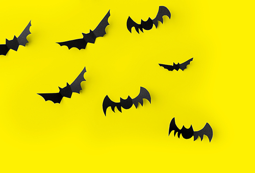 halloween, decoration and scary concept - flock of black paper bats flying over yellow background