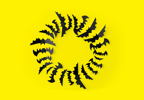 halloween, decoration and scary concept - flock of black paper bats flying over yellow background