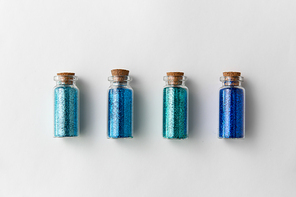 party, decoration and holidays concept - glitters of different blue shades in small glass bottles with cork stoppers over white background