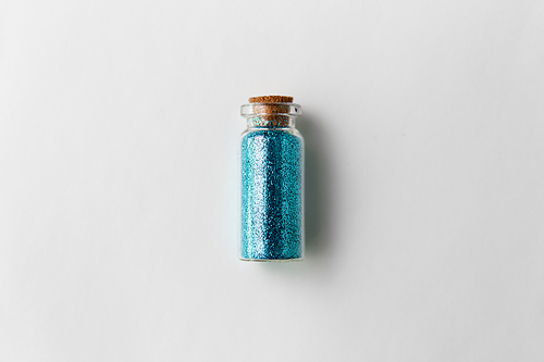 party, decoration and holidays concept - blue glitters in small glass bottle with cork stopper over white background