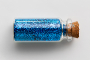 party, decoration and holidays concept - blue glitters in small glass bottle with cork stopper over white background