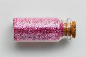 party, decoration and holidays concept - pink glitters in small glass bottle with cork stopper over white background