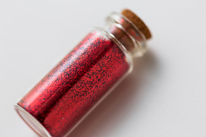 party, decoration and holidays concept - close up of red glitters in small glass bottle with cork stopper over white background