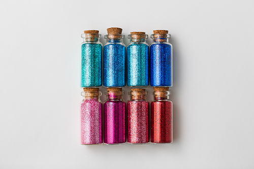 party, decoration and holidays concept - set of different color glitters in small glass bottles with cork stoppers over white background