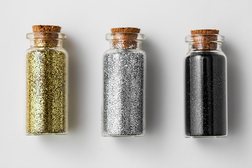 party, decoration and holidays concept - set of gold, silver and black metallic glitters in small glass bottles with cork stoppers over white background