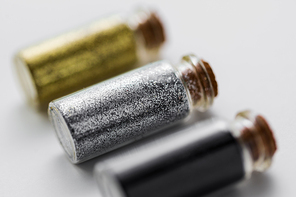 party, decoration and holidays concept - close up of gold, silver and black metallic glitters in small glass bottles with cork stoppers over white background