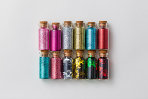 party, decoration and holidays concept - set of different color glitters in small glass bottles with cork stoppers over white background