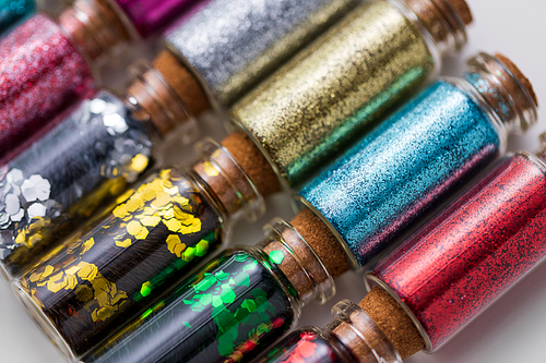 party, decoration and holidays concept - close up of different color glitters in small glass bottles with cork stoppers
