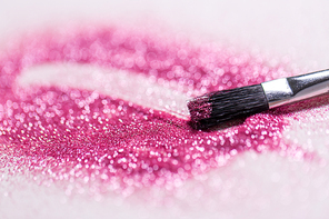 party, decoration and holidays concept - close up of make up brush making stroke on pink glitters on white background