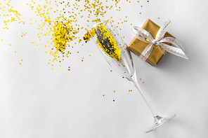 christmas, holidays and celebration concept - champagne wine glass, gift box and golden glitters on white background