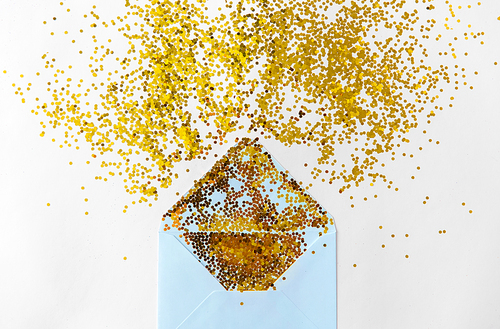 party, decoration and holidays concept - golden glitters and envelope on white background