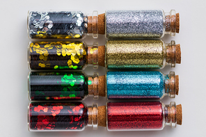 party, decoration and holidays concept - set of different color glitters in small glass bottles with cork stoppers over white background