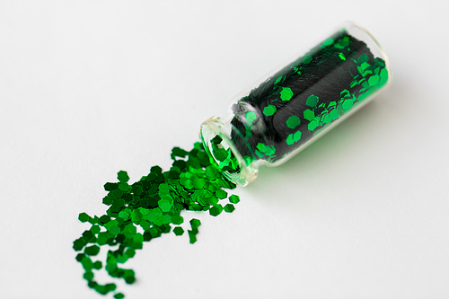 party, decoration and holidays concept - green hexagonal glitters poured from small glass bottle over white background