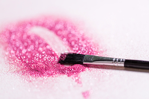 party, decoration and holidays concept - close up of make up brush making stroke on pink glitters on white background