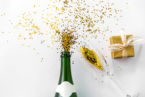 christmas, holidays and celebration concept - champagne bottle, wine glass, gift box and golden glitters on white background