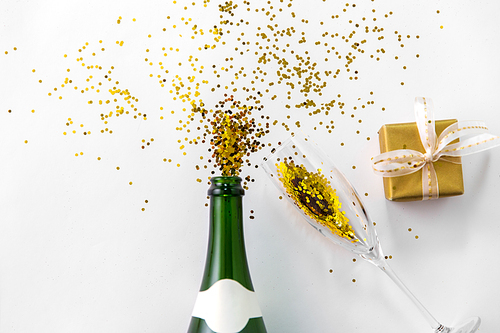 christmas, holidays and celebration concept - champagne bottle, wine glass, gift box and golden glitters on white background