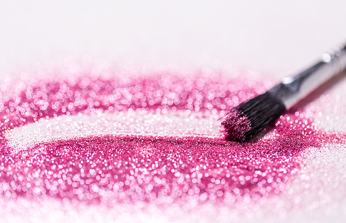 party, decoration and holidays concept - close up of make up brush making stroke on pink glitters on white background