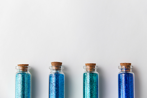 party, decoration and holidays concept - glitters of different blue shades in small glass bottles with cork stoppers over white background