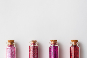 party, decoration and holidays concept - glitters of different red and pink shades in small glass bottles with cork stoppers over white background